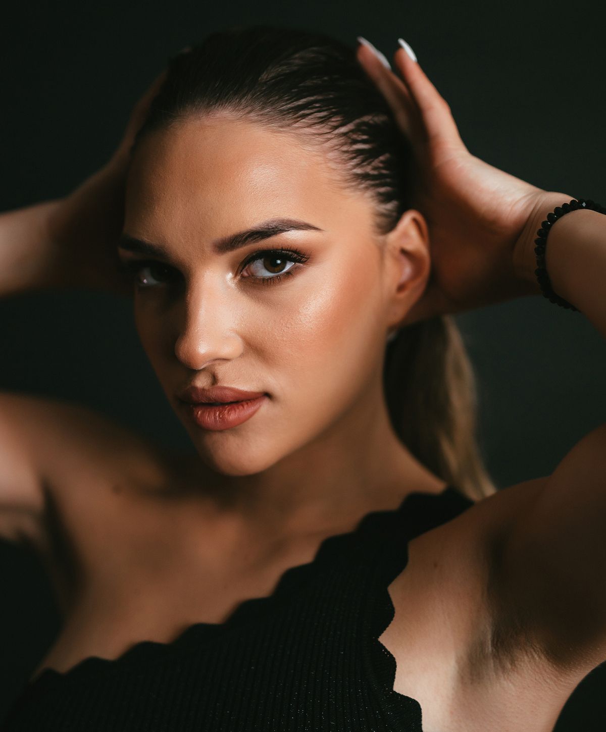 Woman holding hair, posed against dark background.
